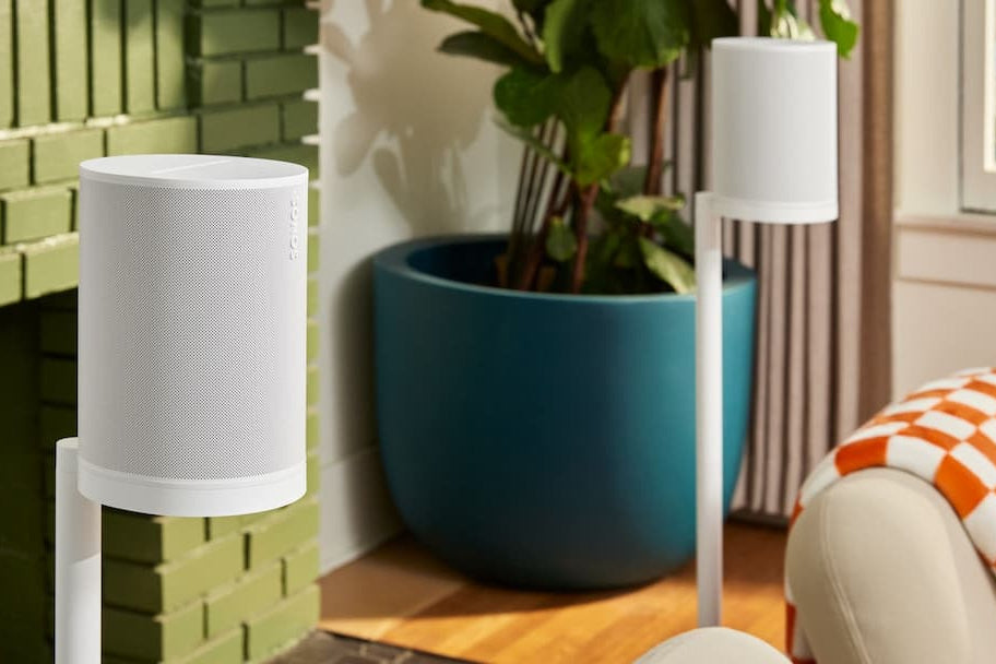 White cylindrical lamp on a green brick wall with a plant and colorful chair in the background