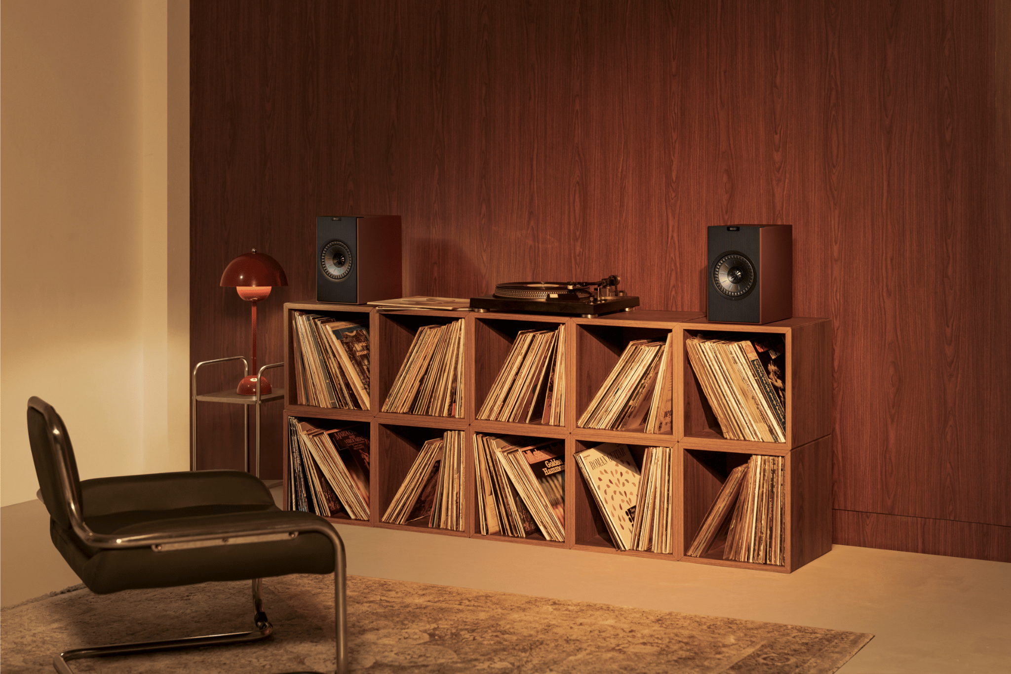 Wooden record player and vinyl collection against a wooden wall with a modern chair.